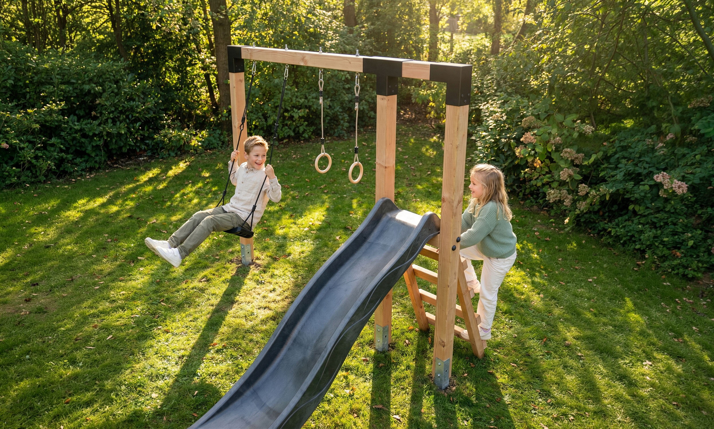 Twee kinderen spelen in de tuin op een houten speeltoestel met schommel, ringen en zwarte glijbaan.